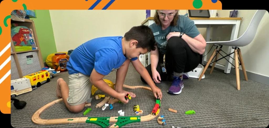Kredo Health therapist and child building a wooden train track together on the clinic floor